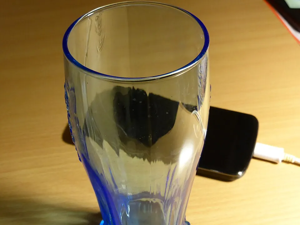 木のテーブルの上のコップと、充電中のスマートフォン