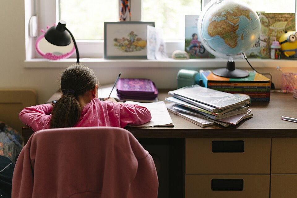 窓辺の机で、背中を向けて勉強する子どもと地球儀