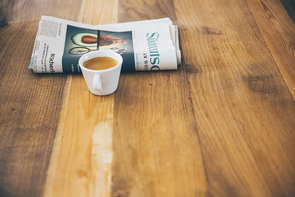 木のテーブルに置かれた新聞とコーヒー
